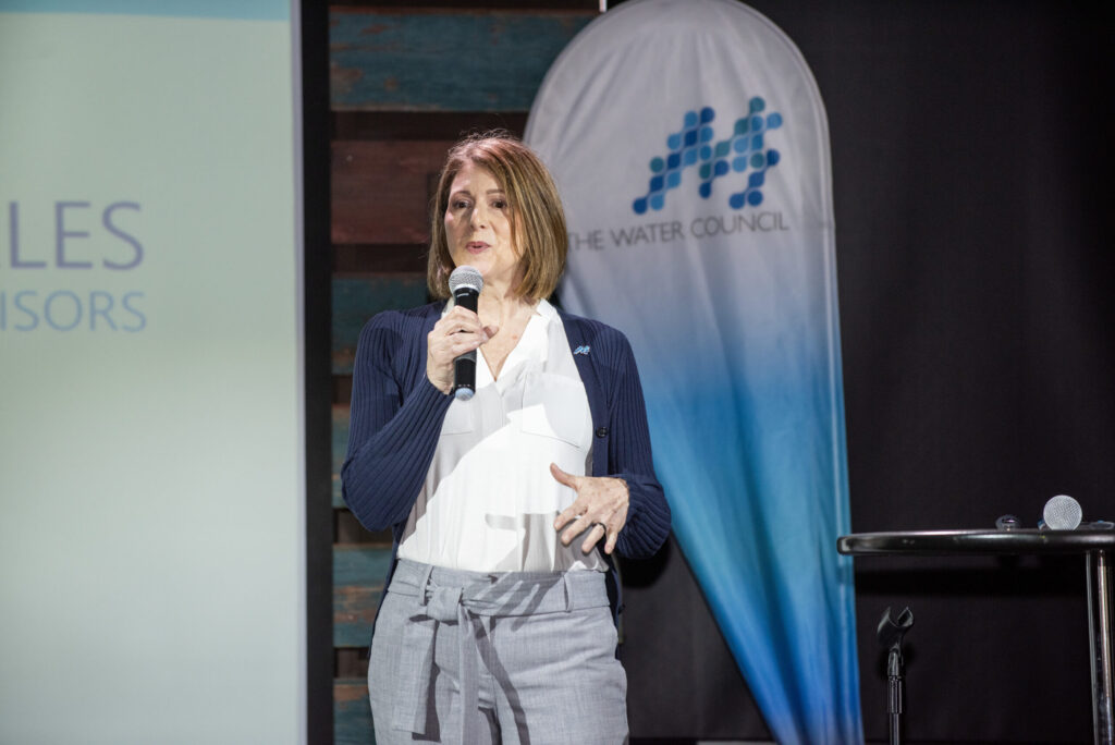 Woman with microphone stands in front of projector screen