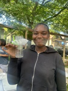 Teen girl holds up water filter she made using a coffee filter and water bottle.