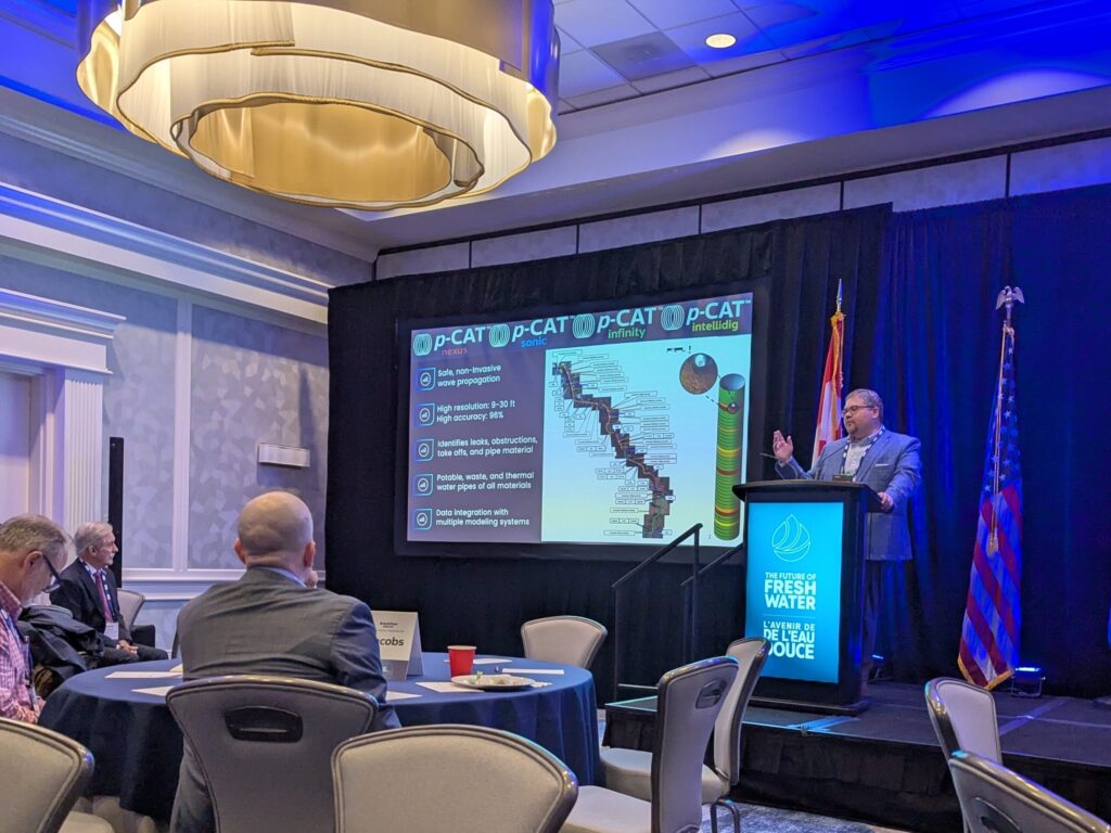 Man stands at a lectern giving a presentation with a slideshow behind him.