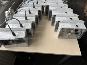 11 rectangular alarm boxes with white tops and clear fronts showing electronic workings inside.