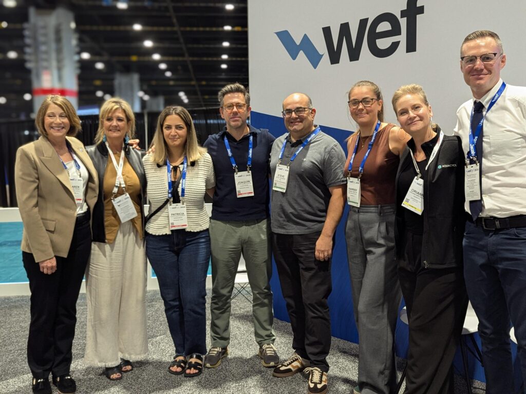 A group of WEFTEC attendees pose in front of a wall that says WEFTEC