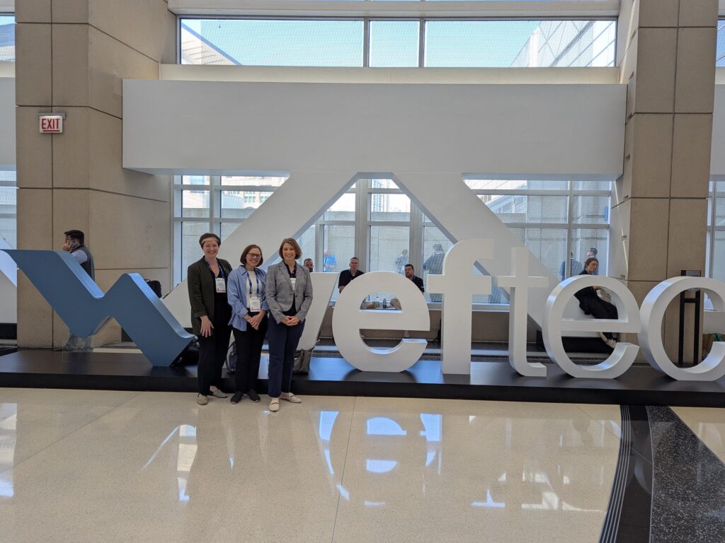 Three women stand in front of large letter sculptures that spell out WEFTEC.