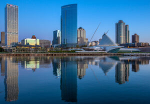 Skyscrapers and the Milwaukee Art Museum, a white building shaped like a ship, face Lake Michigan and are reflected in the water.