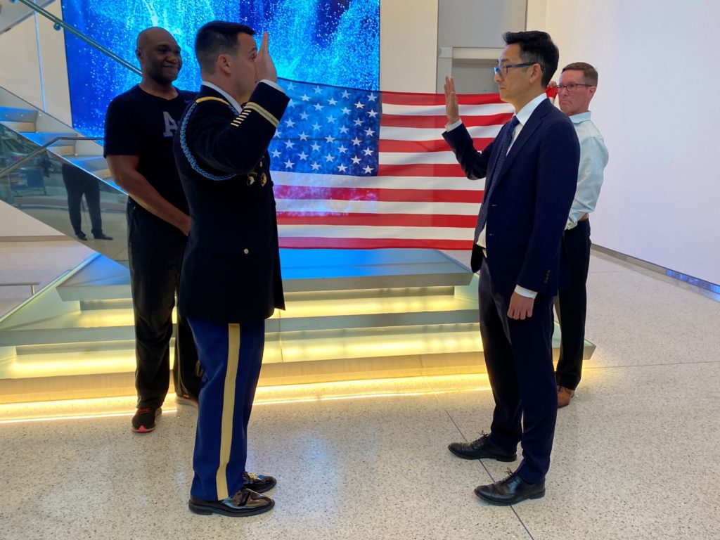 Man in suit is sworn in by Army officer in uniform with American flag in background