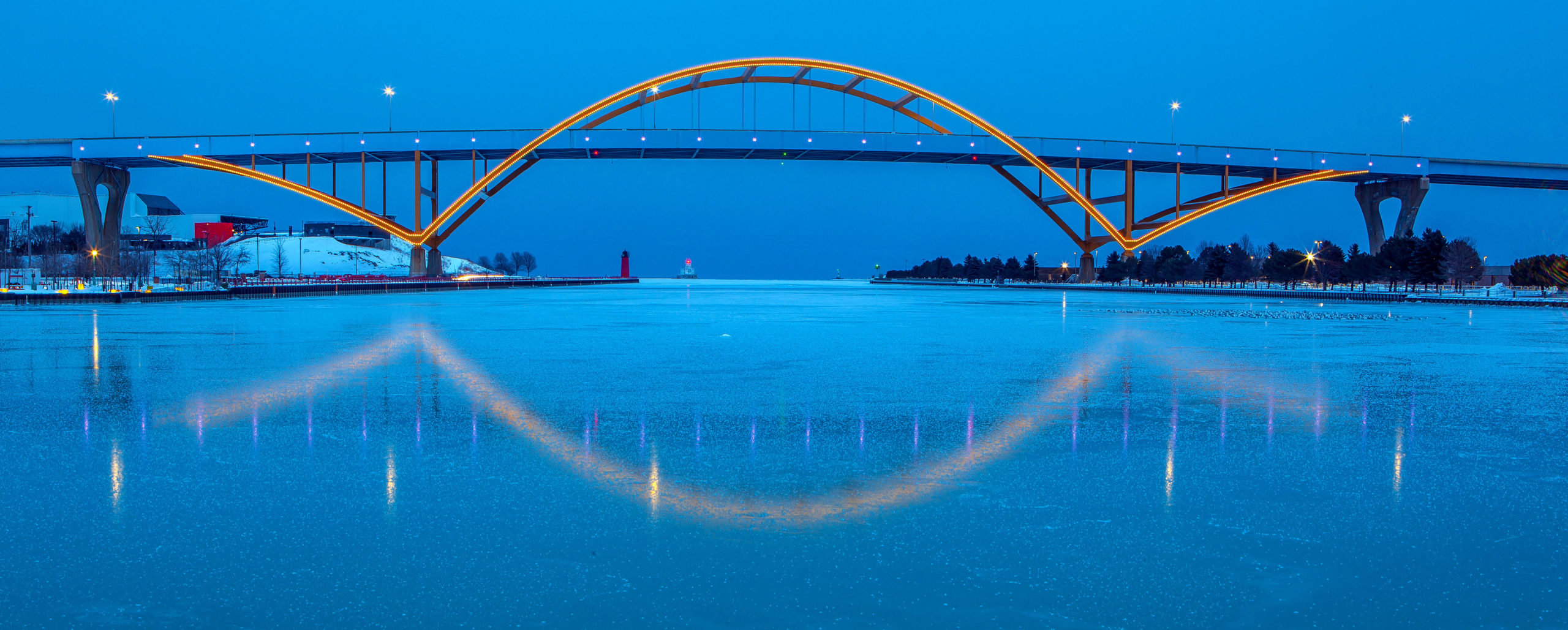 Bridge with large yellow arch over icy lake at dusk