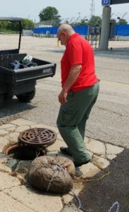 Man in red shirt stands over open sewer