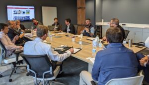 Businesspeople talk around a conference table with a TV screen in back