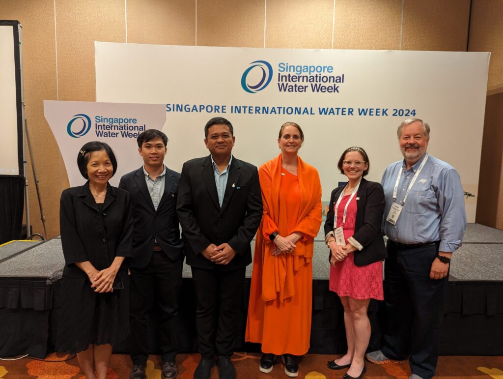 Six people pose for a photo in front of a Singapore International Water Week backdrop.