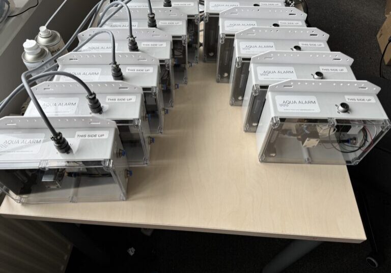 11 rectangular alarm boxes with white tops and clear fronts showing electronic workings inside.