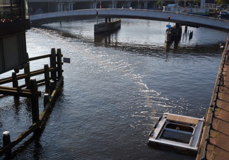 Photo of a river with a bridge across it. A square device on the bank of the river releases bubbles across the river.