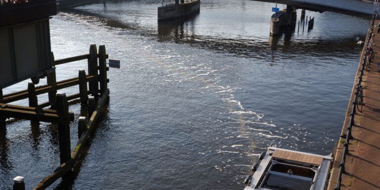 Photo of a river with a bridge across it. A square device on the bank of the river releases bubbles across the river.