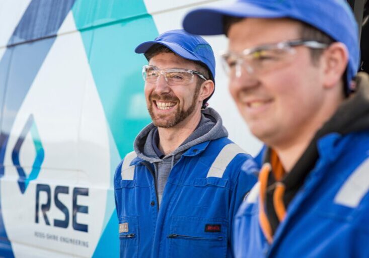 Two men in blue hats in front of van with RSE logo