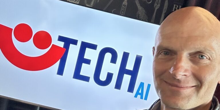 Man smiles in front of banner with red smiley face (Summerfest logo) that says TECH AI.