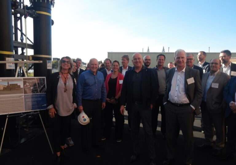 Crowd of people pose for photo outside next to wastewater treatment equipment.