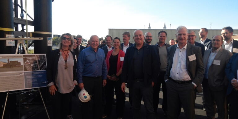 Crowd of people pose for photo outside next to wastewater treatment equipment.