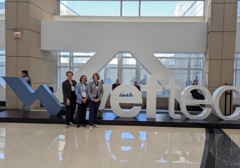 Three women stand in front of large letter sculptures that spell out WEFTEC.