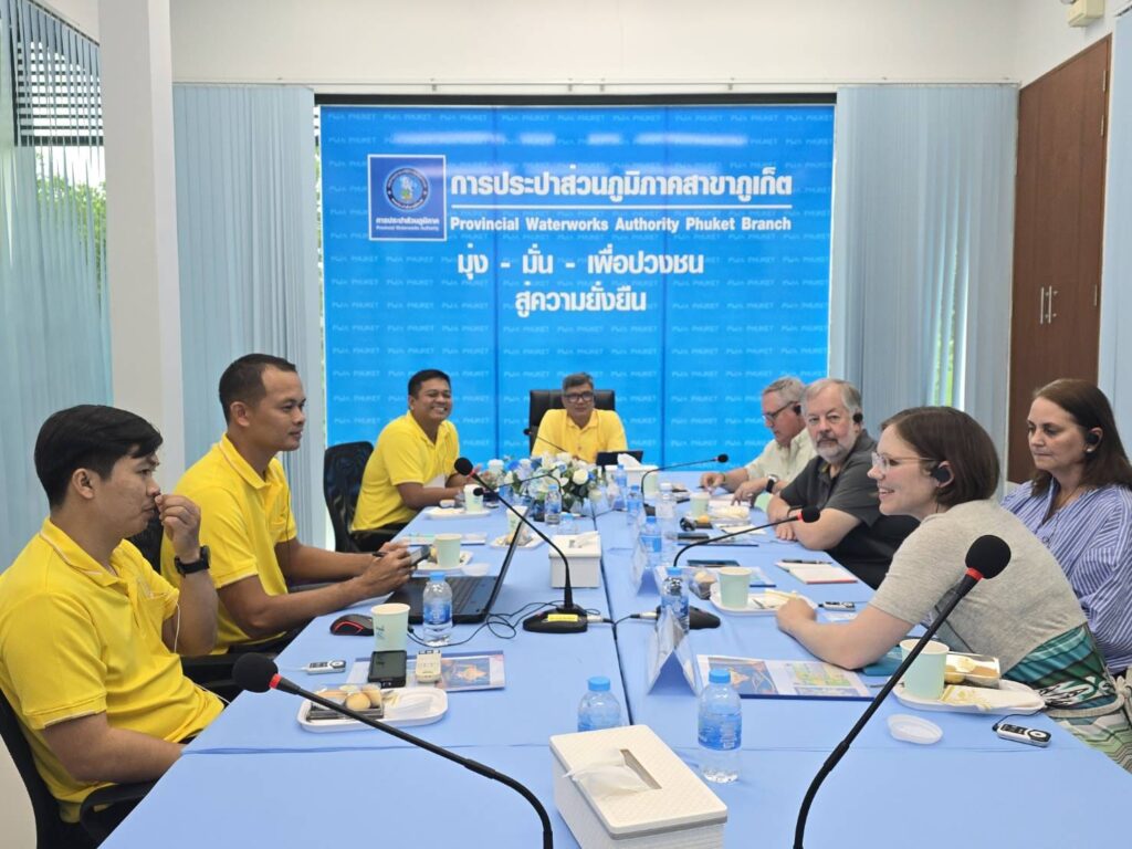 People sit around a long table with microphones and a blue screen in the background.